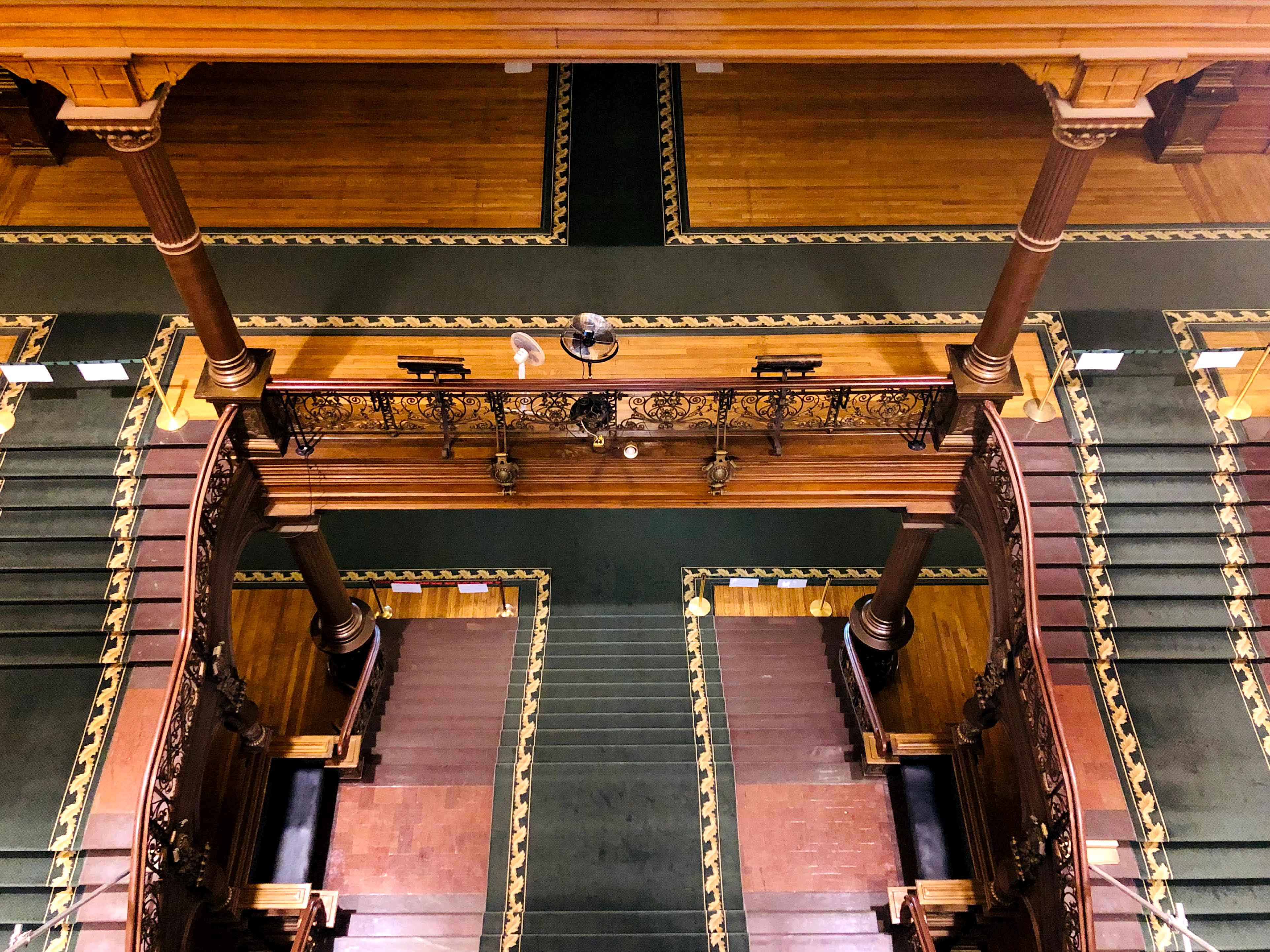 Une vue de haut en bas du grand escalier montrant les deux niveaux, les colonnes et la ferronnerie.