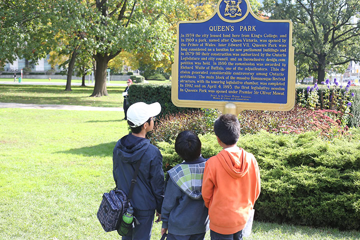 three children looking at a plaque for Queen's Park