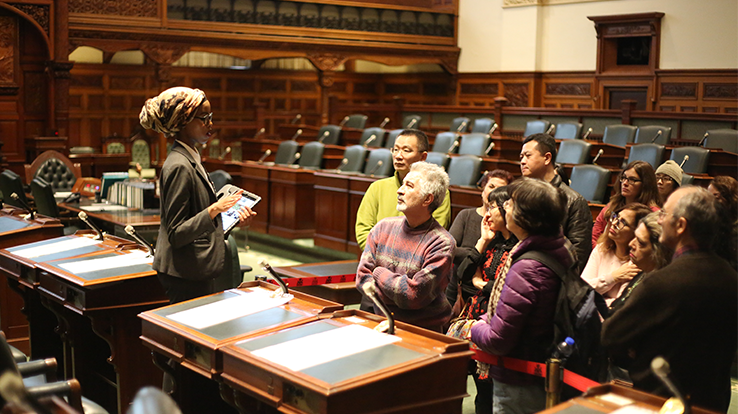 a tour guide speaks to a group of people inside the Legislative Chamber