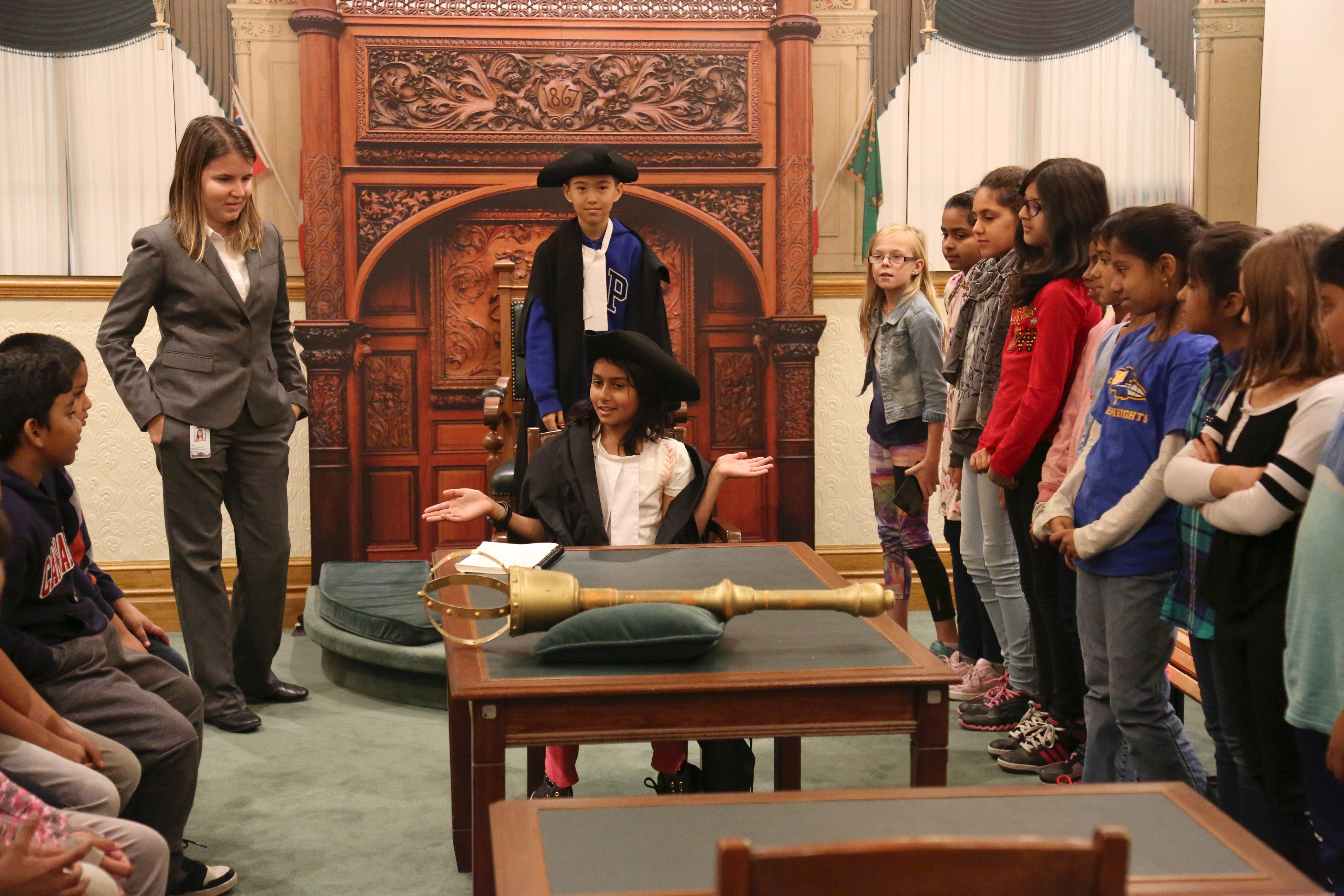 Group of young students surrounding a table with the Mace on top. Two students are in Parliamentary uniform acting as the Speaker and the Clerk.