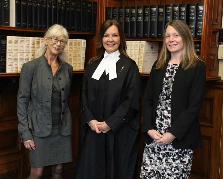 La présidente et deux femmes qui posent devant une bibliothèque.