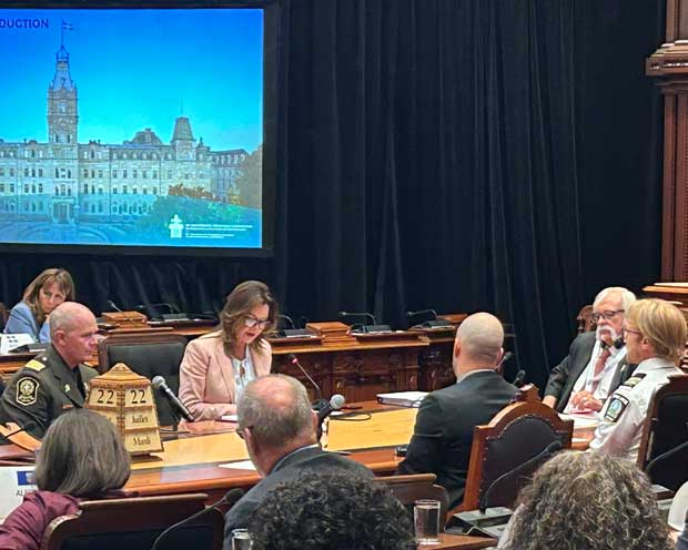 La présidente et plusieurs personnes sont assises à une table équipée de microphones