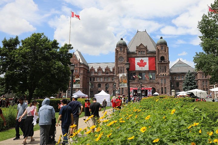 Des personnes marchent sous le soleil vers l’édifice de l’Assemblée législative pendant la Fête du Canada 2025