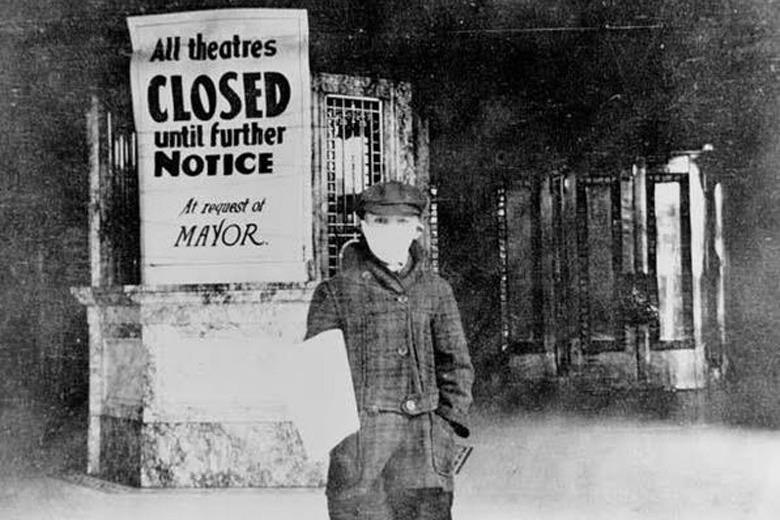 Sur cette photo de 1918, un jeune crieur de journaux se tient, visage masqué, devant la billetterie d’un cinéma. On y a placardé une affiche annonçant en anglais : « Tous les cinémas fermés jusqu’à nouvel ordre à la demande du maire. » 