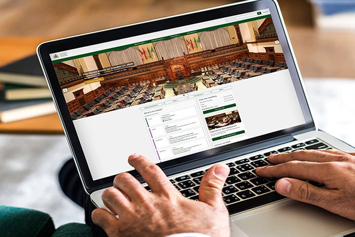 hands resting on a laptop keyboard with a screen displaying the Legislative Assembly of Ontario's website home page