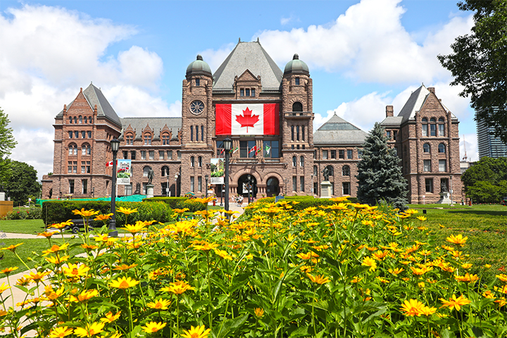 The Legislative Building pictured in the background on a sunny summer day with a garden of yellow flowers in the foreground.