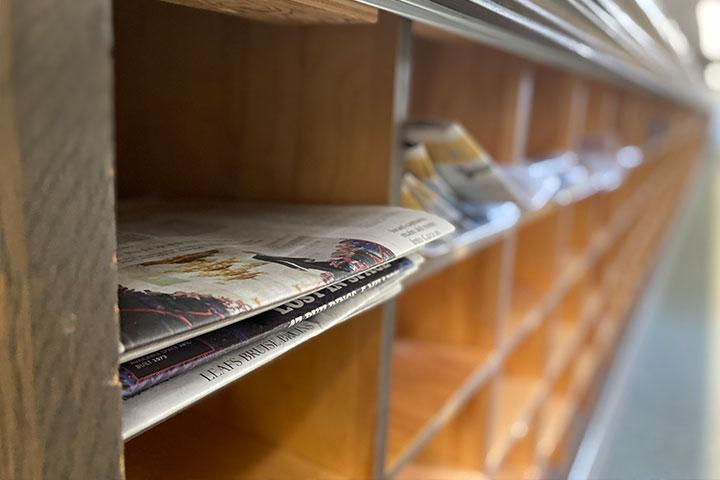 A stack of newspapers placed on a wooden shelf.