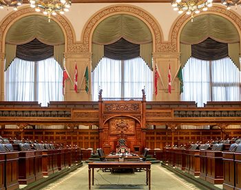 Empty Legislative Chamber with desks, chandeliers, and three large windows