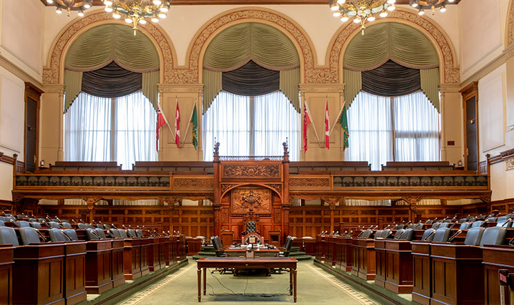 empty Legislative Chamber with desks, chandeliers, and three large windows