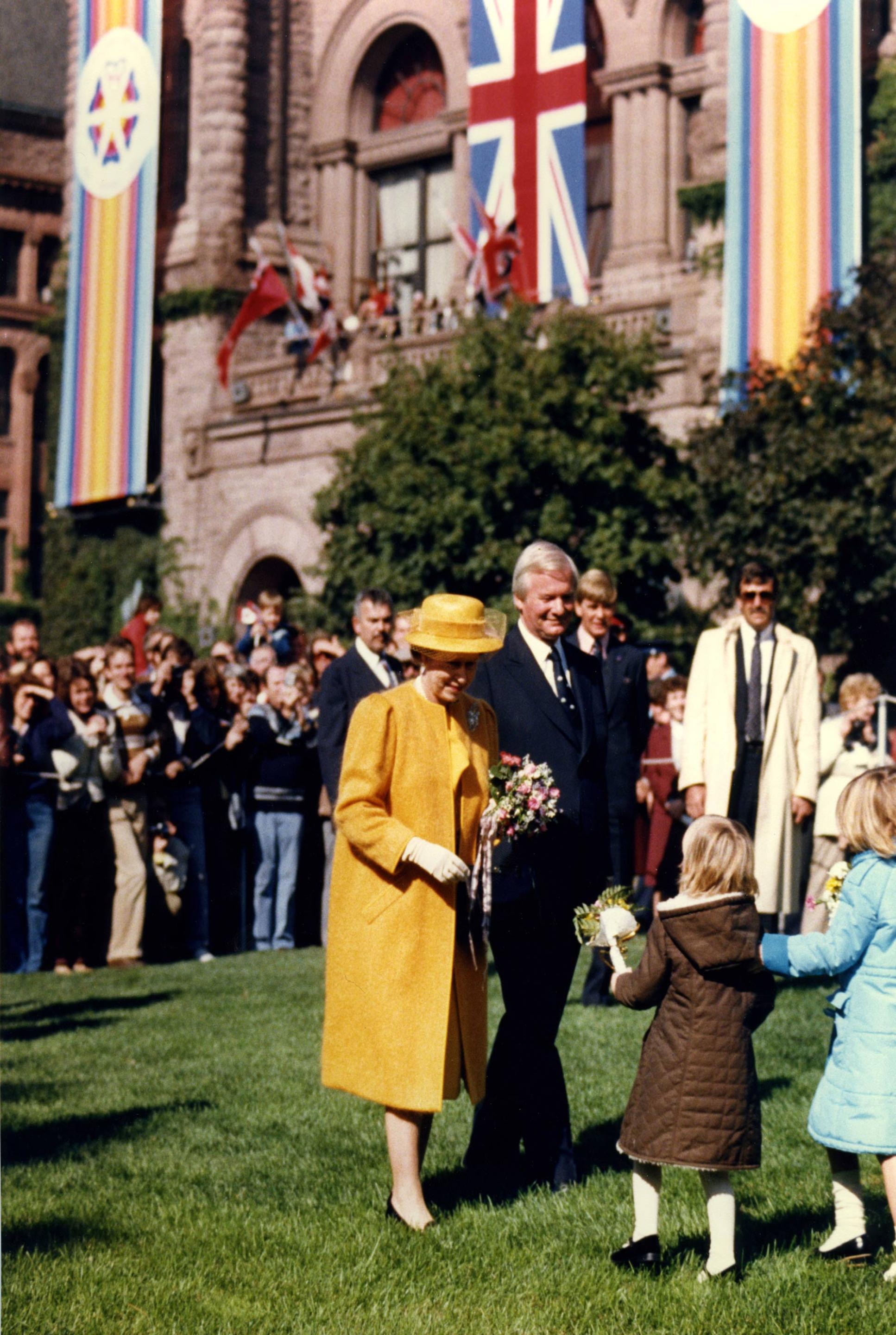 Her Majesty Queen Elizabeth II accepts flowers from several young girls during a 1984 visit to Queen's Park