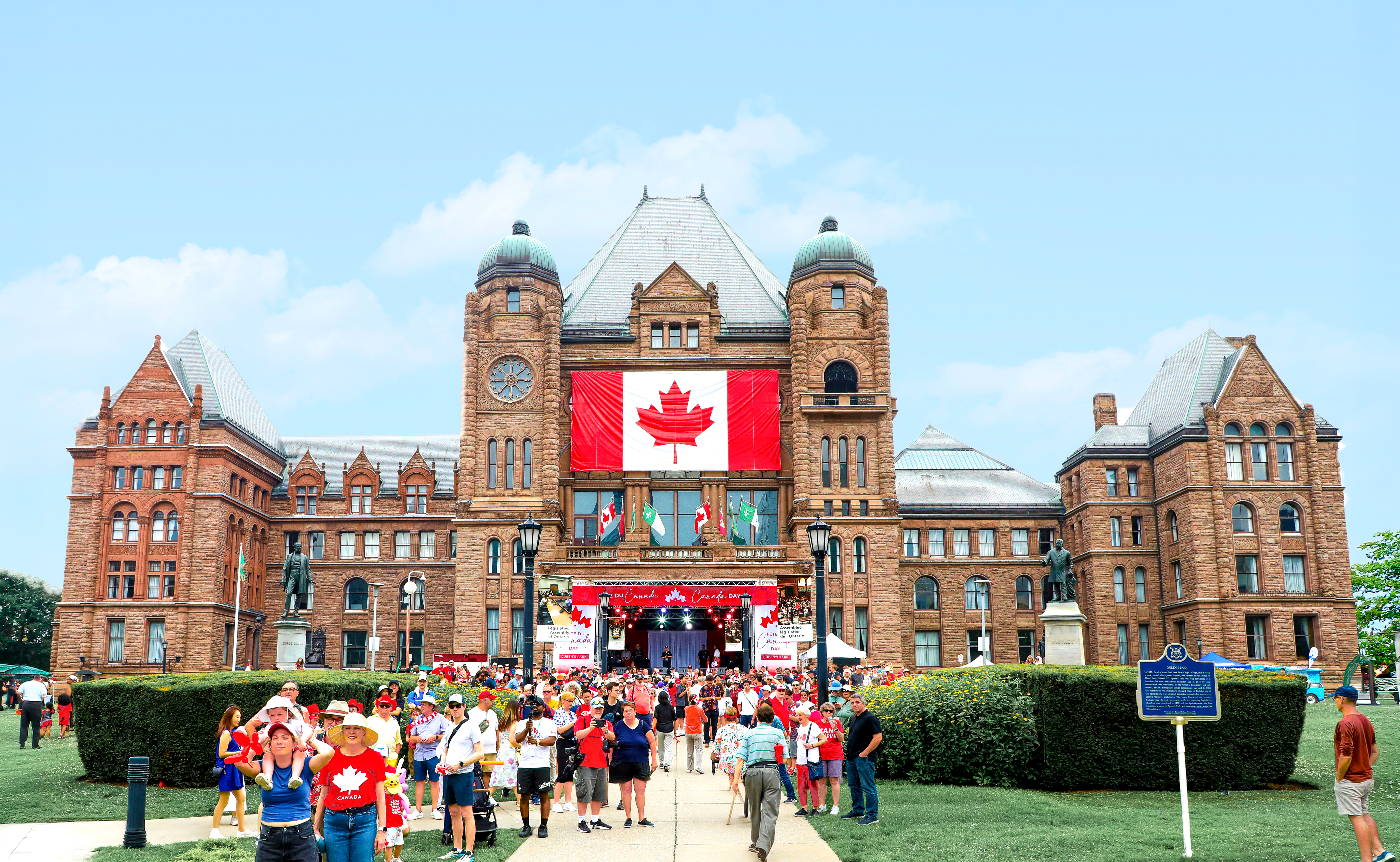 Des personnes marchent sous le soleil vers l’édifice de l’Assemblée législative pendant la Fête du Canada 2025