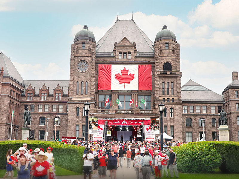Des personnes marchent sous le soleil vers l’édifice de l’Assemblée législative pendant la Fête du Canada 2025