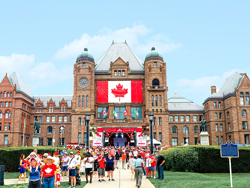 Des personnes marchent sous le soleil vers l’édifice de l’Assemblée législative pendant la Fête du Canada 2025