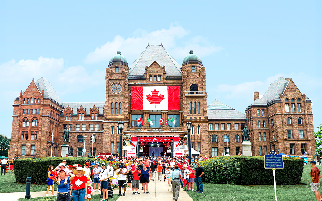 Des personnes marchent sous le soleil vers l’édifice de l’Assemblée législative pendant la Fête du Canada 2025
