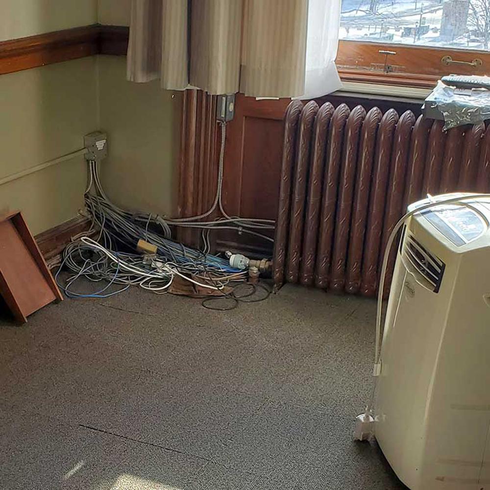 a tangled mass of exposed wires on the floor in the corner of an office